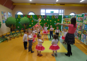 Dzieci ustawione w kole śpiewają piosenkę, unoszą ręce nad głową.